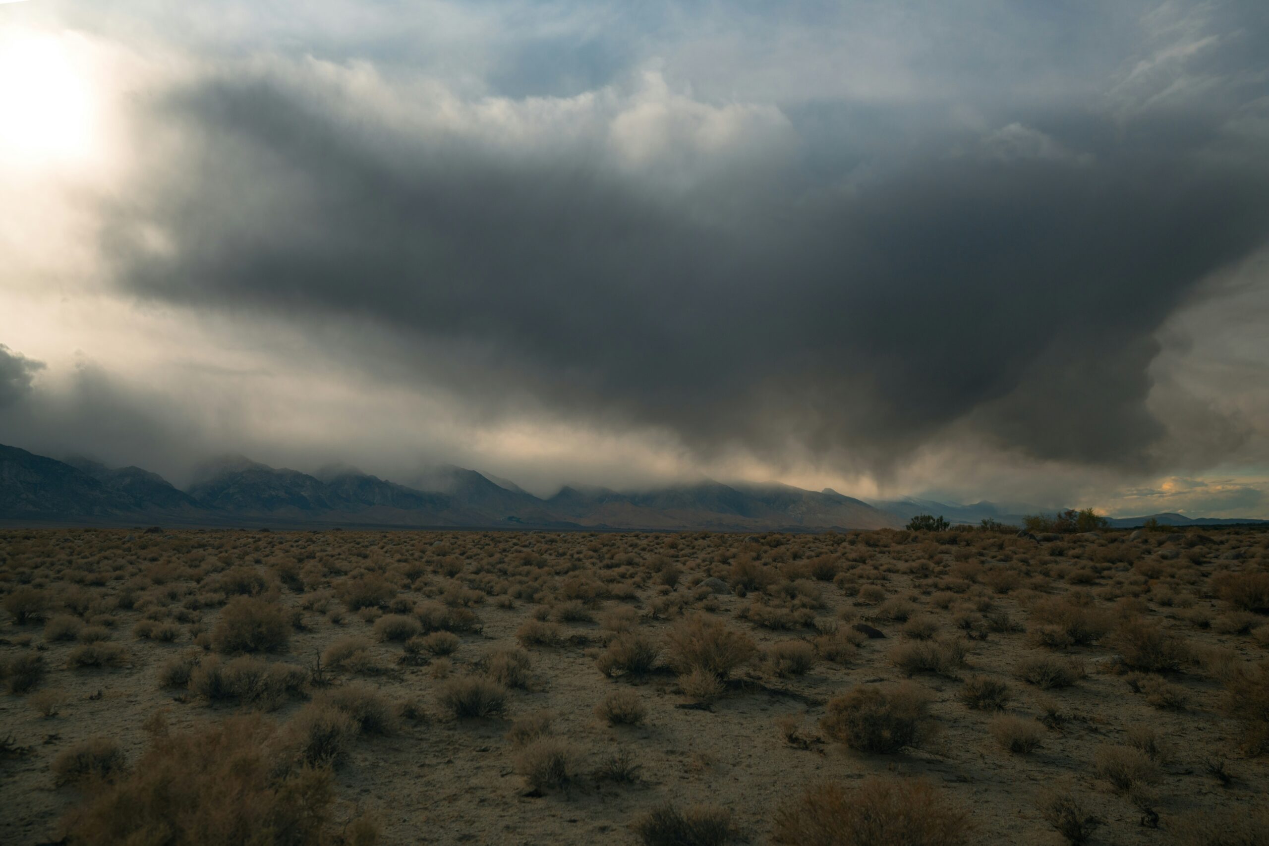 Storm clouds over sagebrush desert with mountains in the distance.